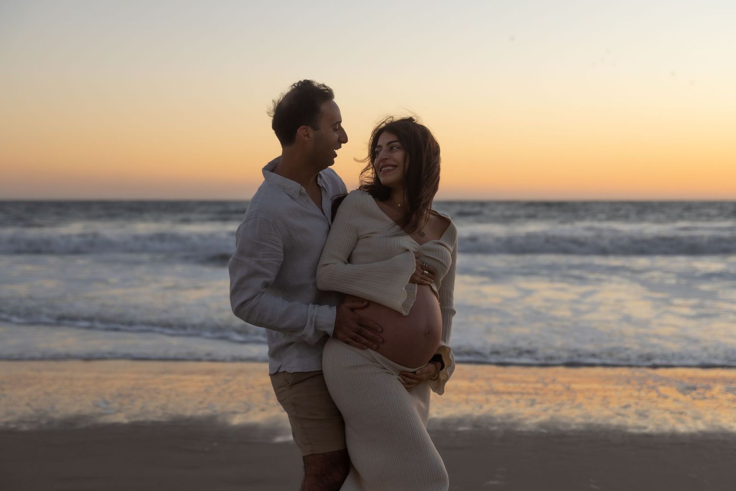 Portrait of a smiling pregnant woman and her husband on the beach at sunset.