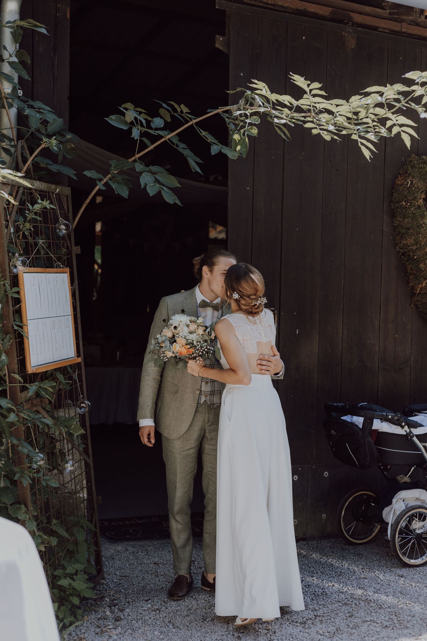 Intimate wedding portrait against dark wooden barn door with greenery.