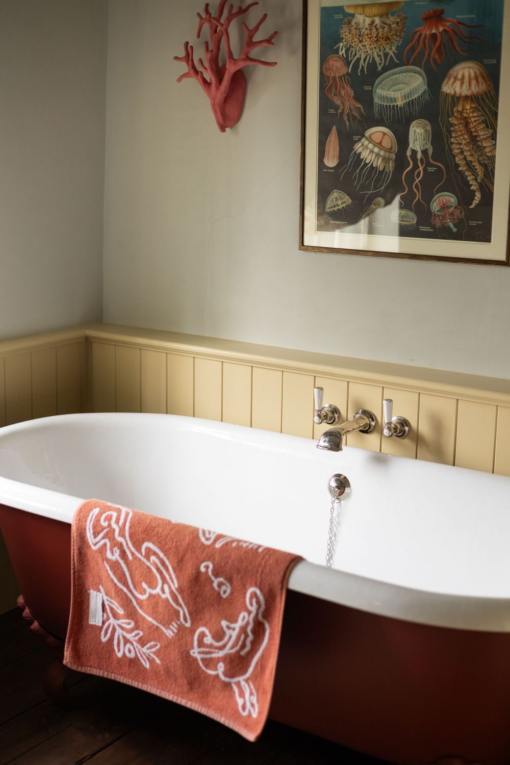 Vintage bathtub with coral towel against white paneling and sea life artwork.