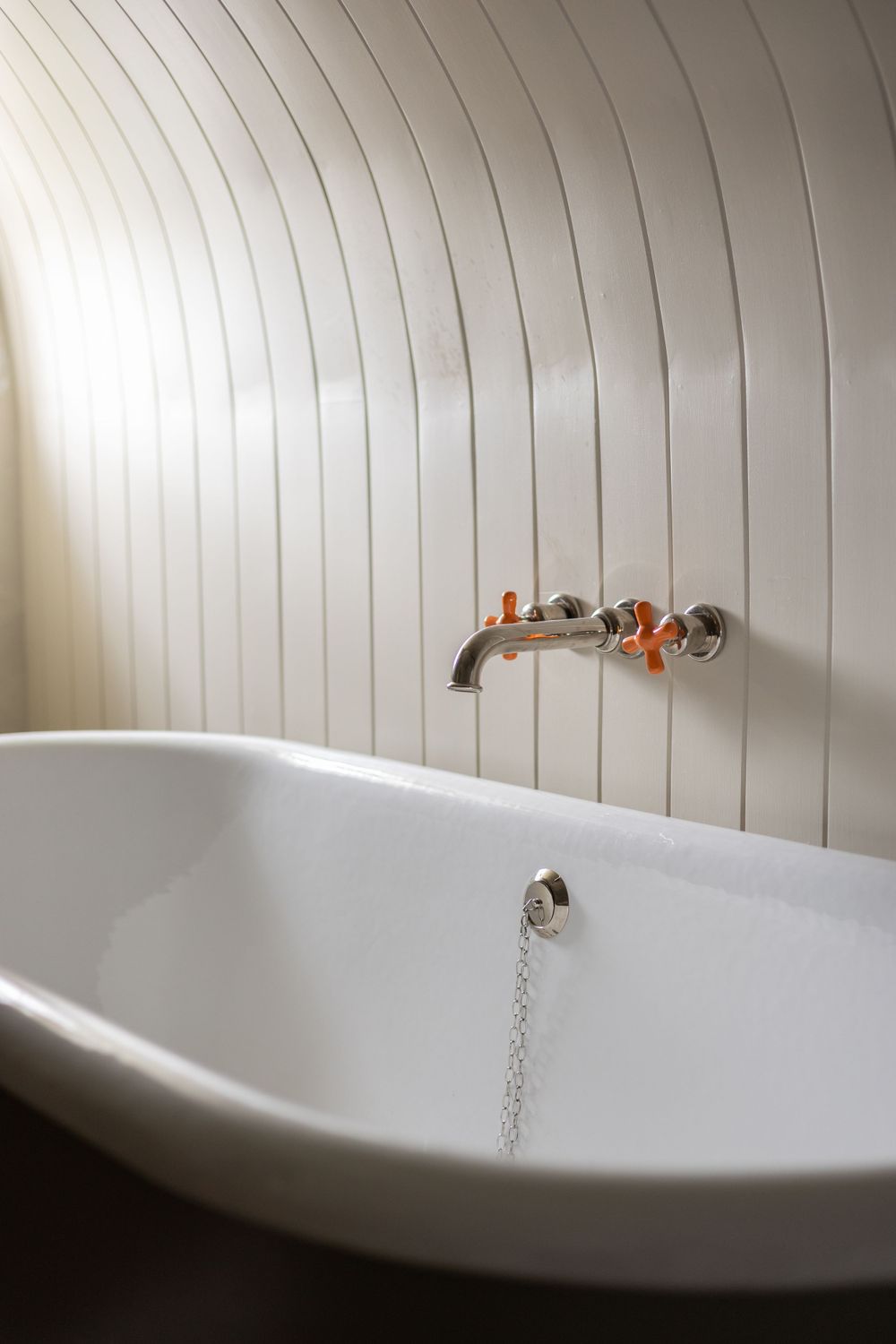 Minimalist white clawfoot bathtub with vertical paneled wall detail.