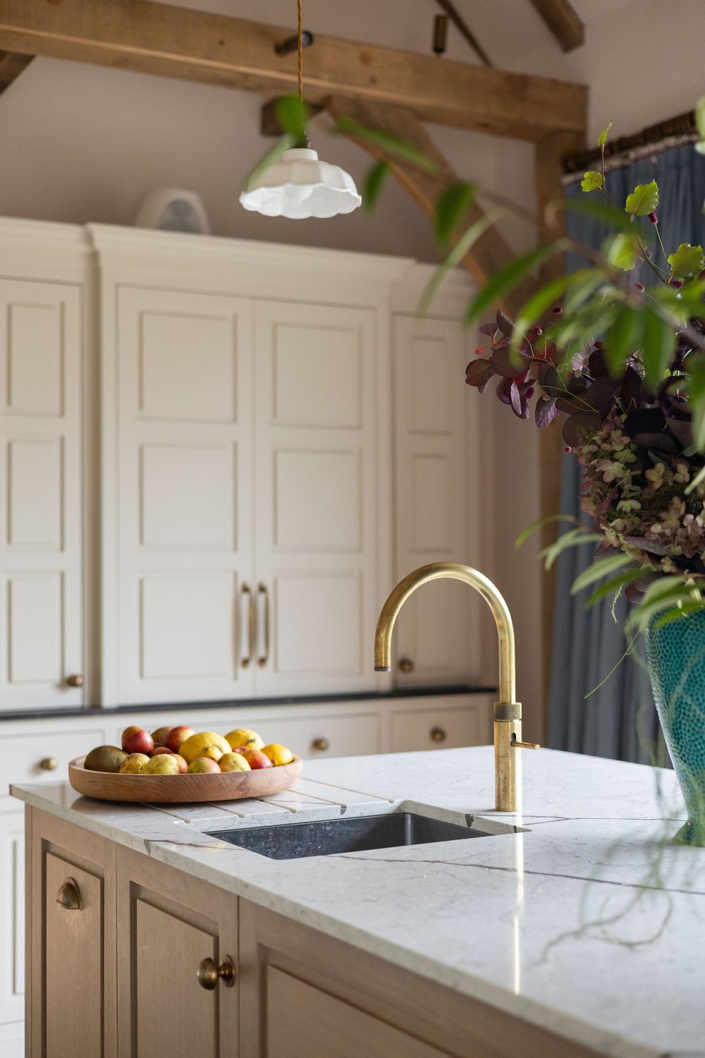 Modern white kitchen with marble countertops, brass fixtures and exposed wooden beams.