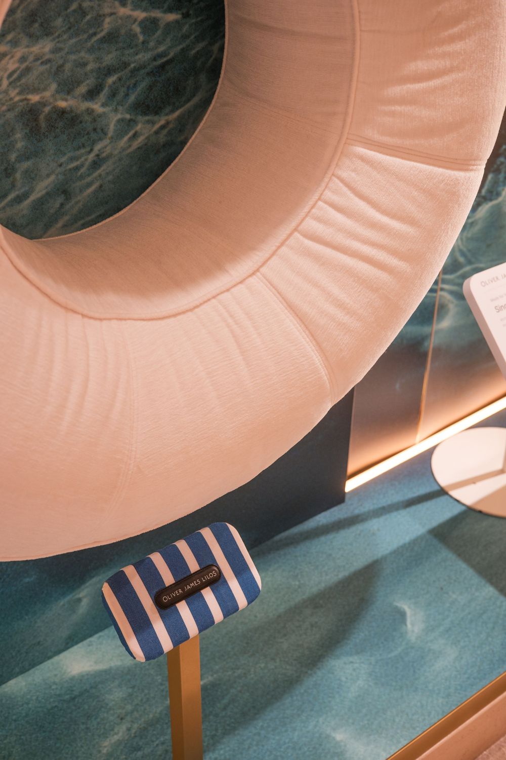 Pink curved seating with striped pillows against a teal wall in a modern space. Harrods exhibition.