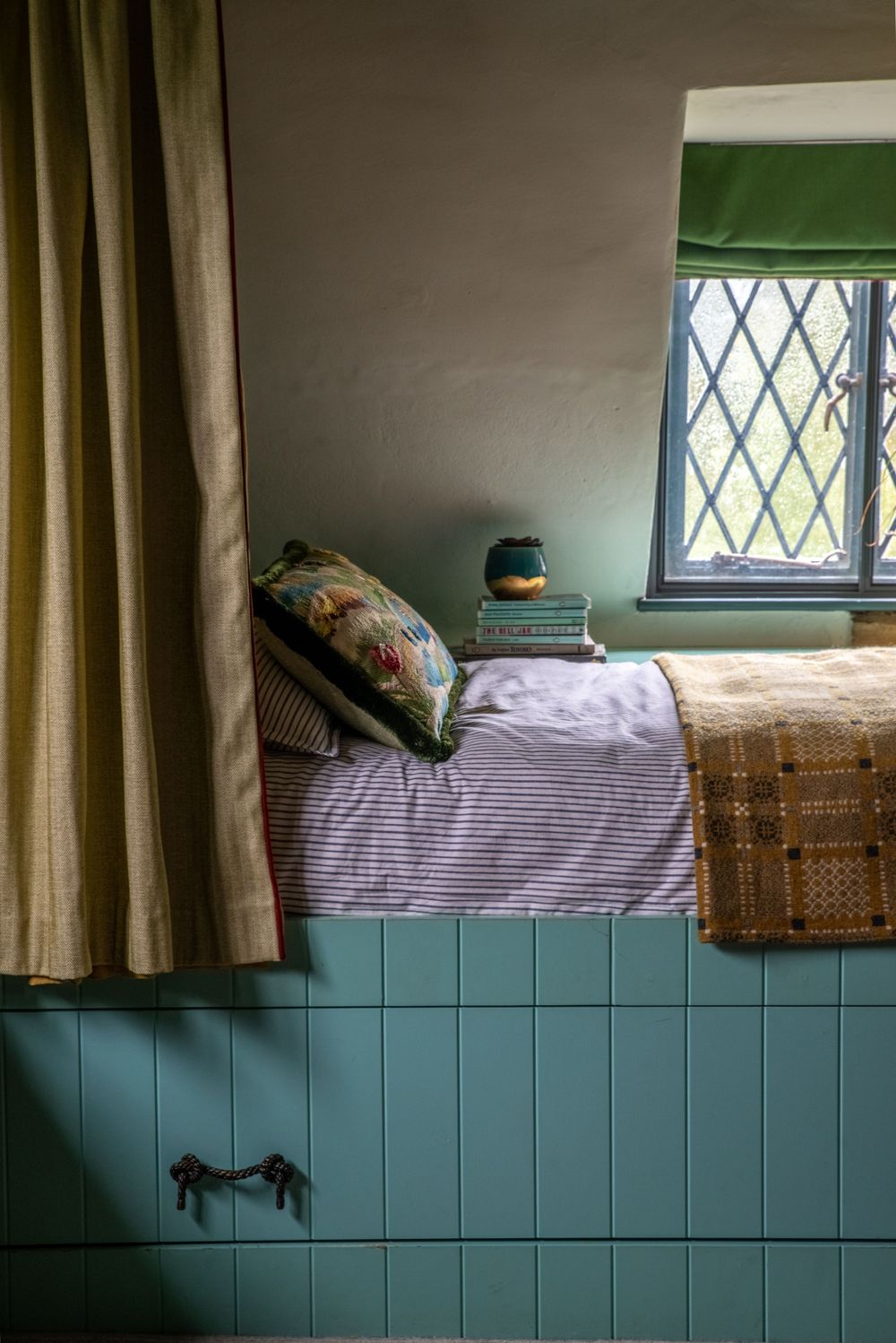 Cozy bedroom nook with diamond-paned window and sage green wainscoting.