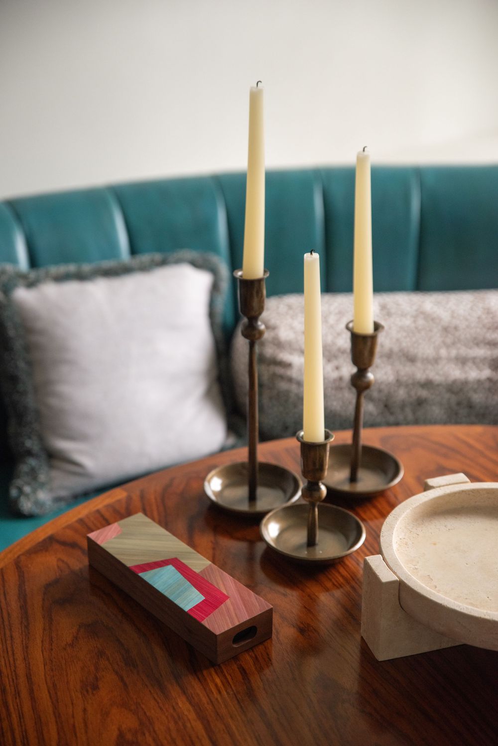 Elegant table setting with tall white candles in brass holders against a teal backdrop.