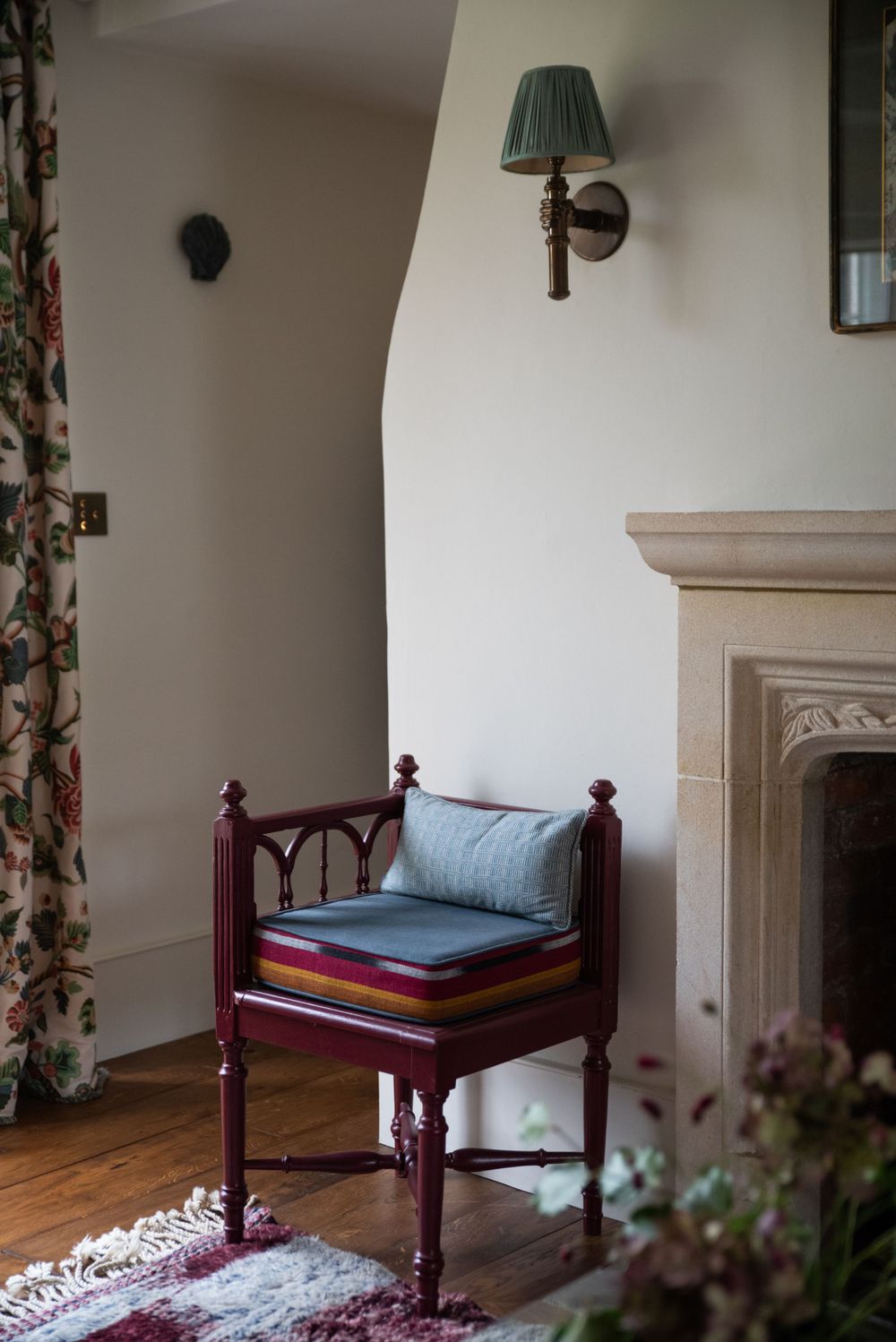 Vintage-style room with floral curtains, wooden bench, and stone fireplace mantel.