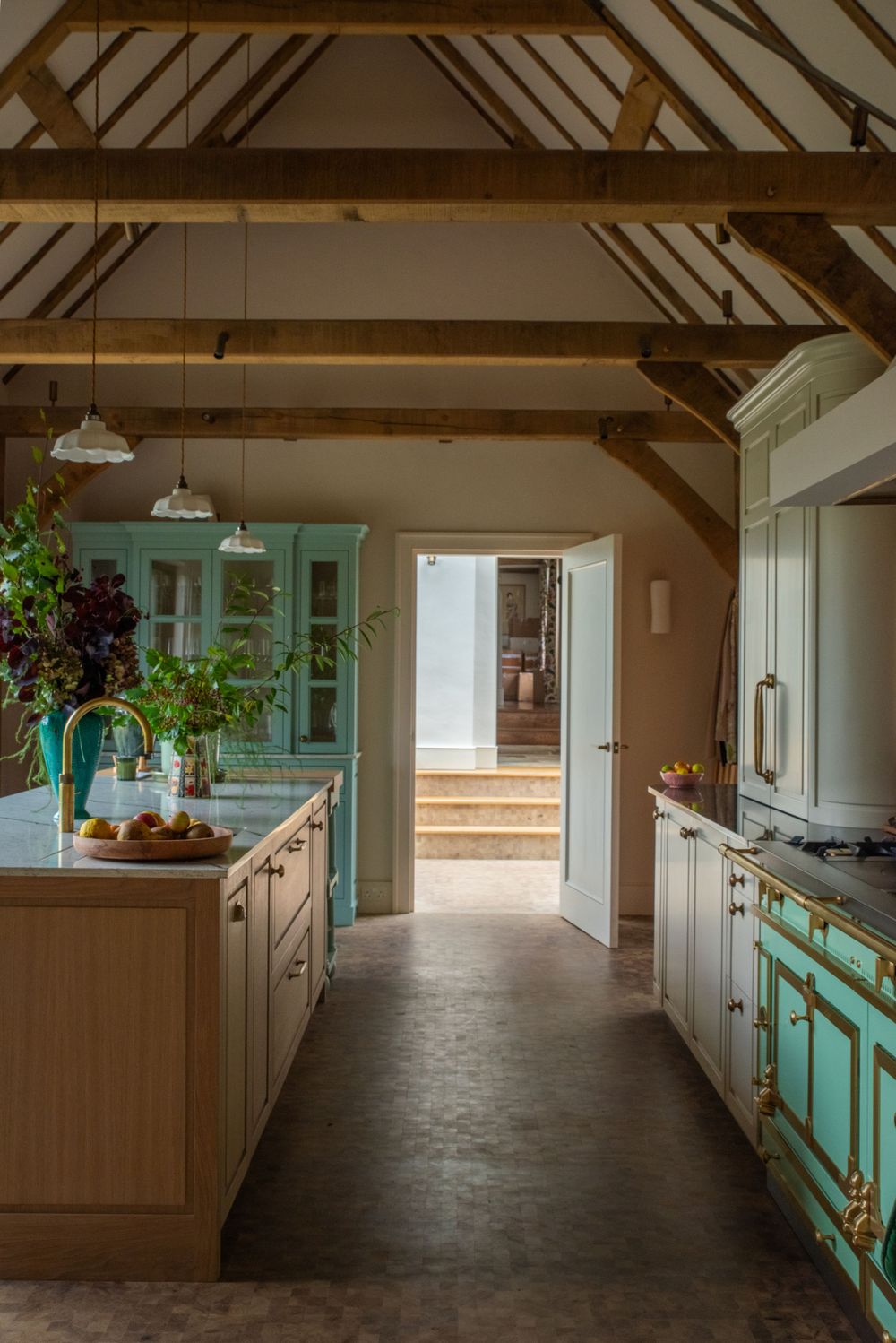 Long kitchen interior with exposed wooden beams and mint green cabinets under natural lighting.