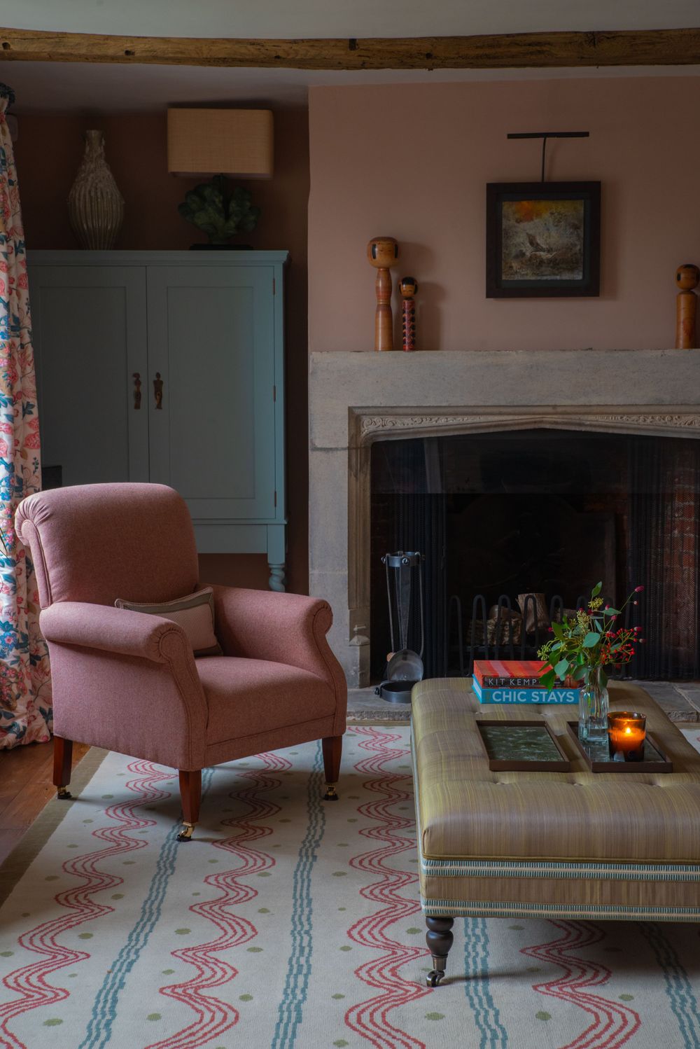 Living room with pink armchair and patterned rug features a traditional fireplace and blue accents.