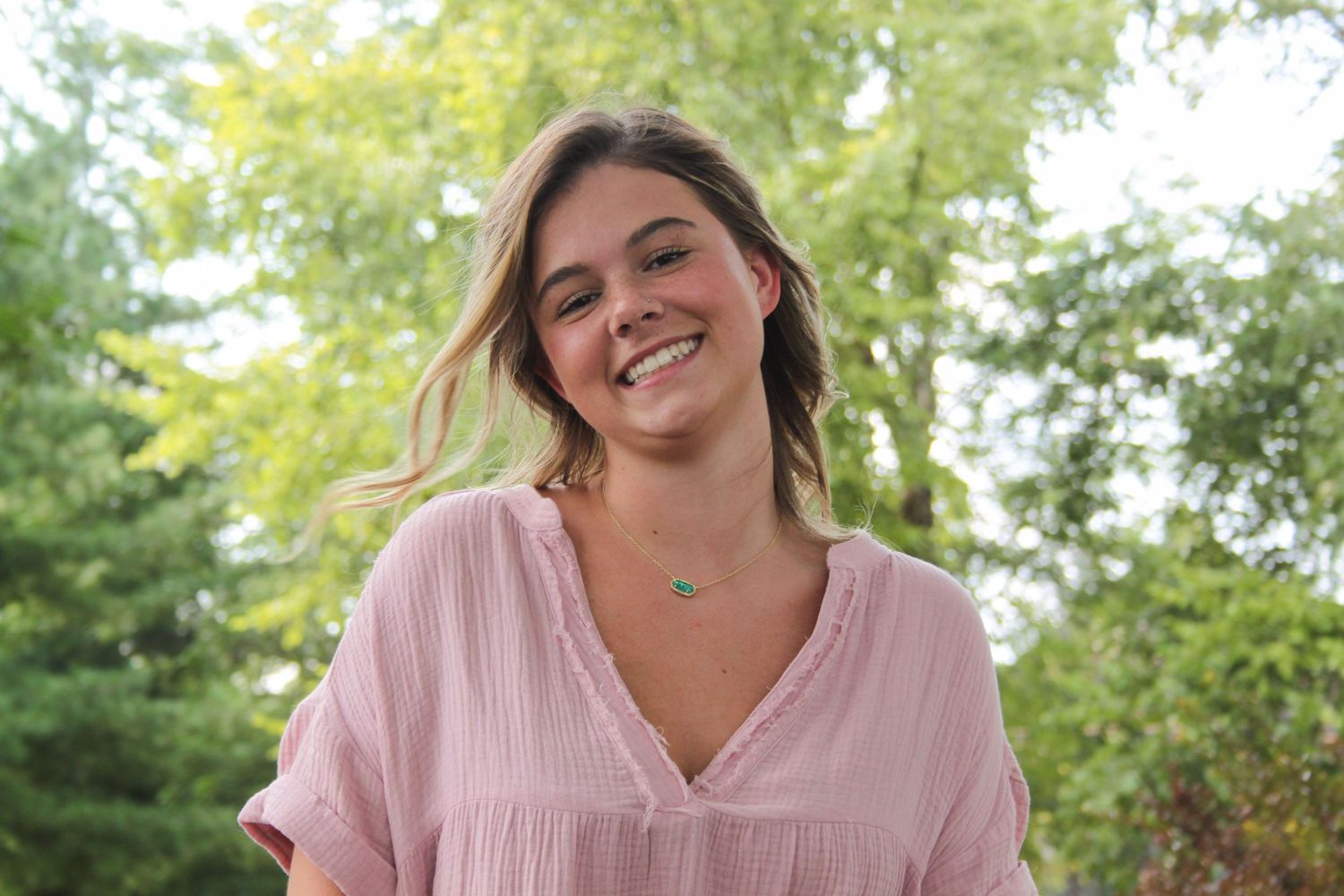 Girl smiling in front of trees for senior pictures.