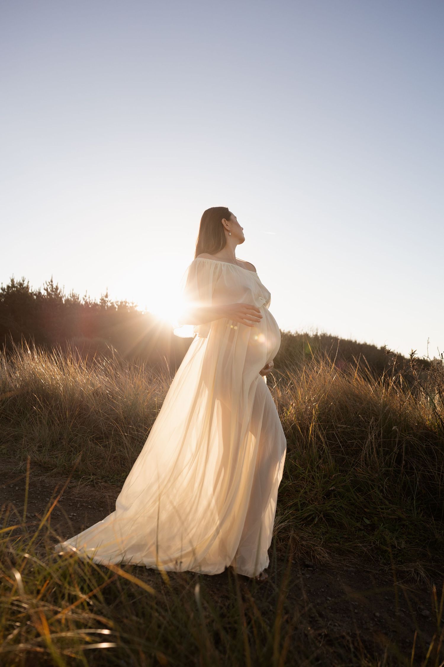 Sunset maternity session, mum holding bump at the beach