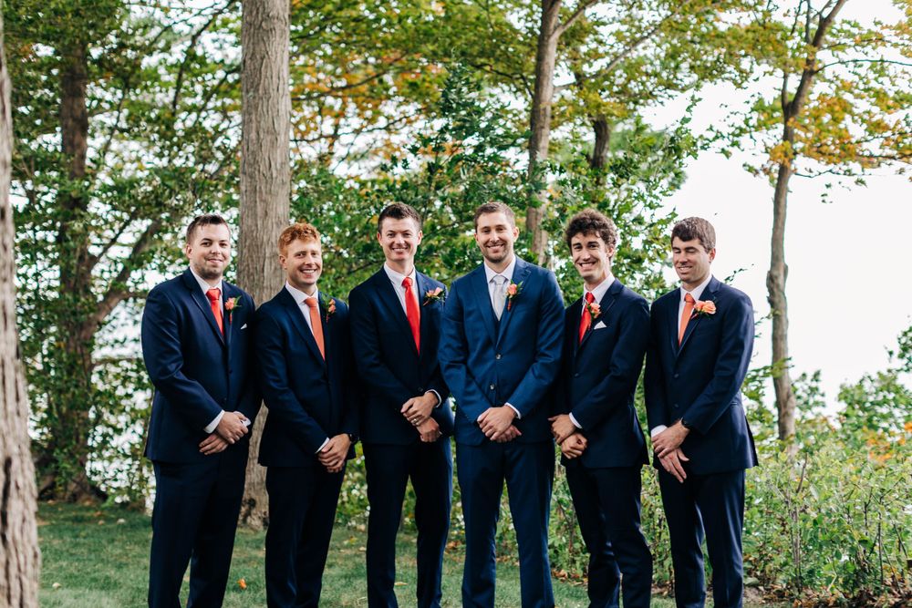 Groomsmen in navy suits with red ties pose together in a wooded setting.