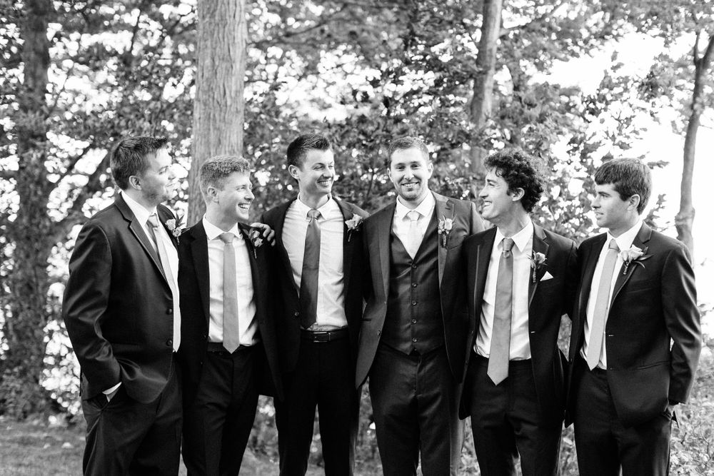 Black and white portrait of groomsmen sharing a casual moment outdoors.