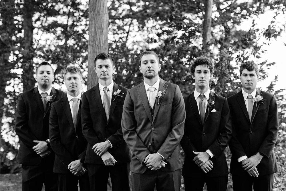 Formal black and white portrait of groomsmen standing in formation against a forest backdrop.