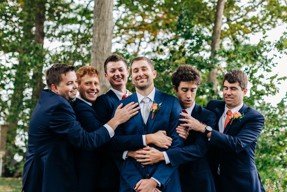 Groomsmen playfully pose with the groom in a fun group photo outdoors.