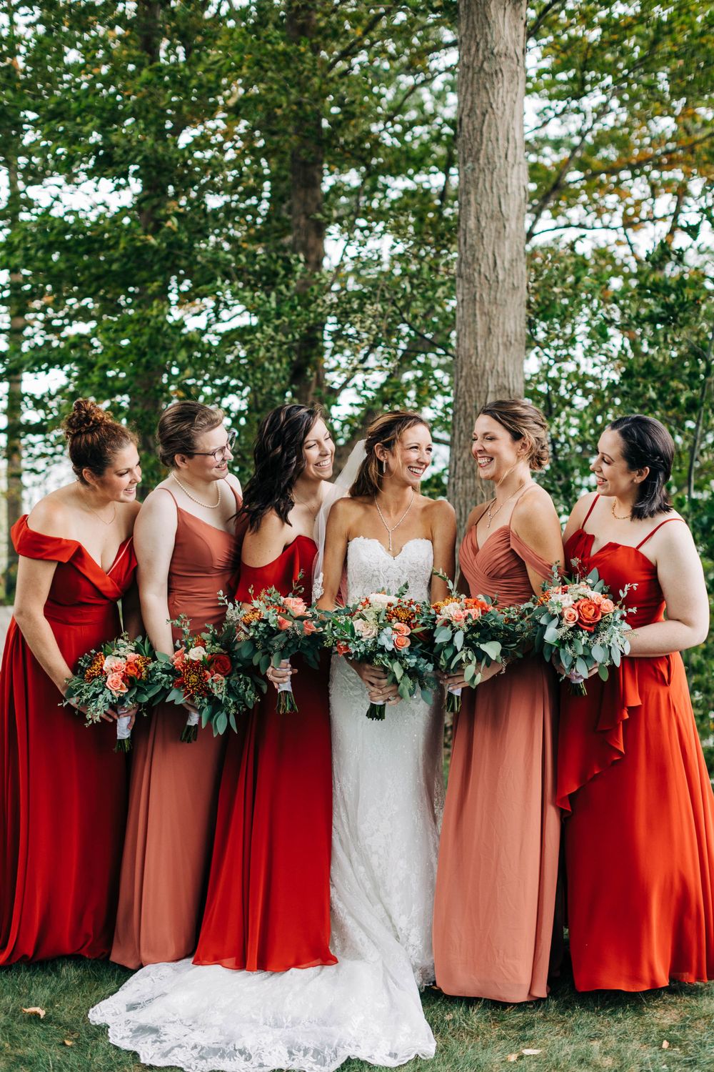Candid moment of bridal party laughing together in complementary red and coral dresses.