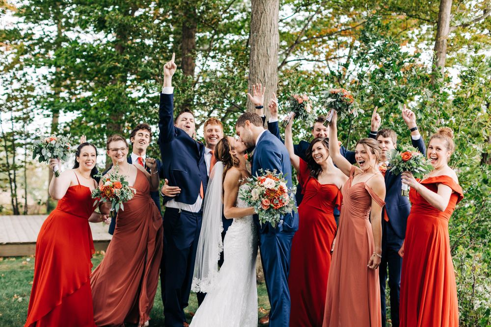 Joyful wedding party celebrates outdoors wearing navy suits and red dresses.