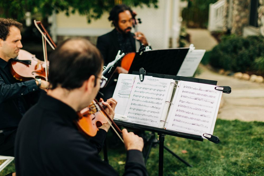 String quartet musicians perform outdoors reading from sheet music stands.