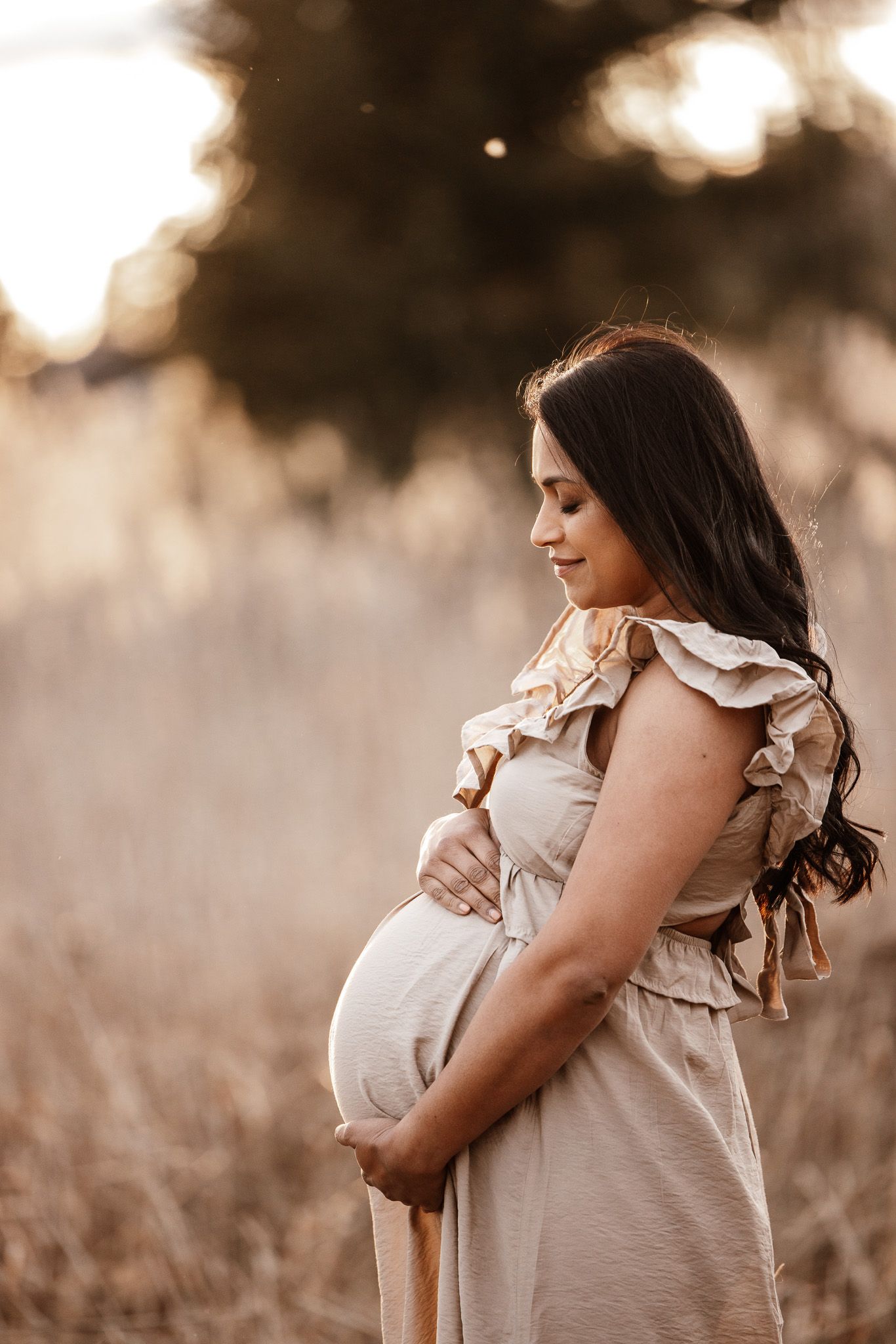 Expectant mother in ruffled dress poses in a field during golden hour.