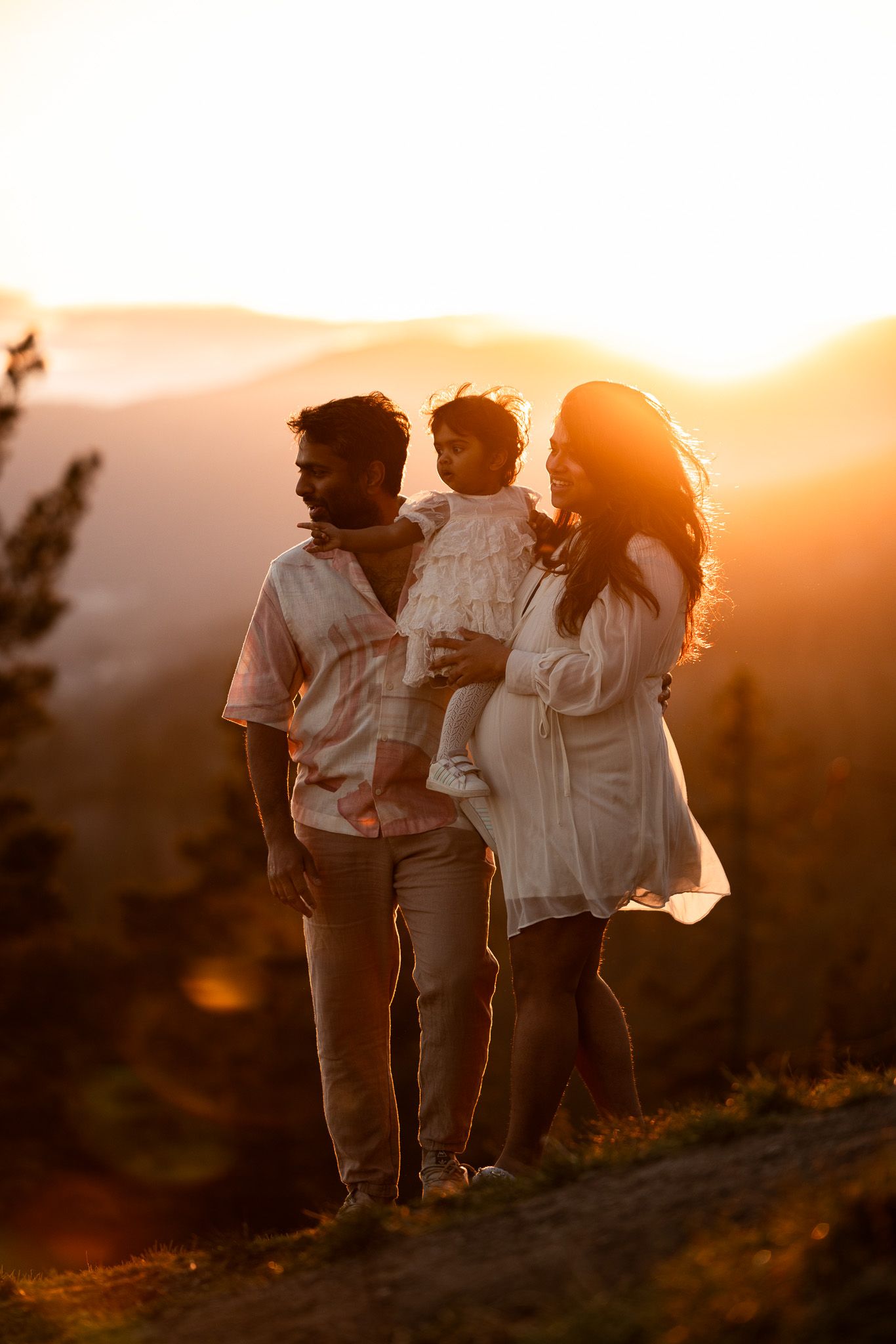 Family of three stands together on hilltop during golden sunset hour.