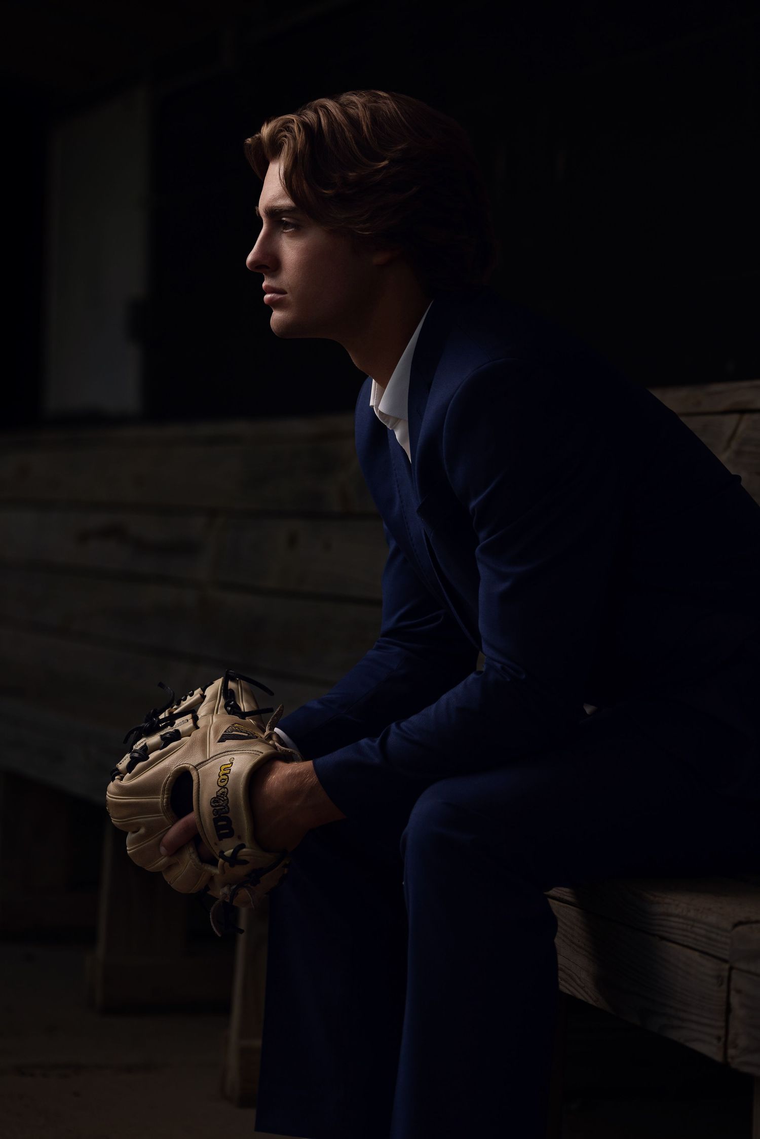 A person in a navy blue suit jacket sits in shadows holding a beige leather football.