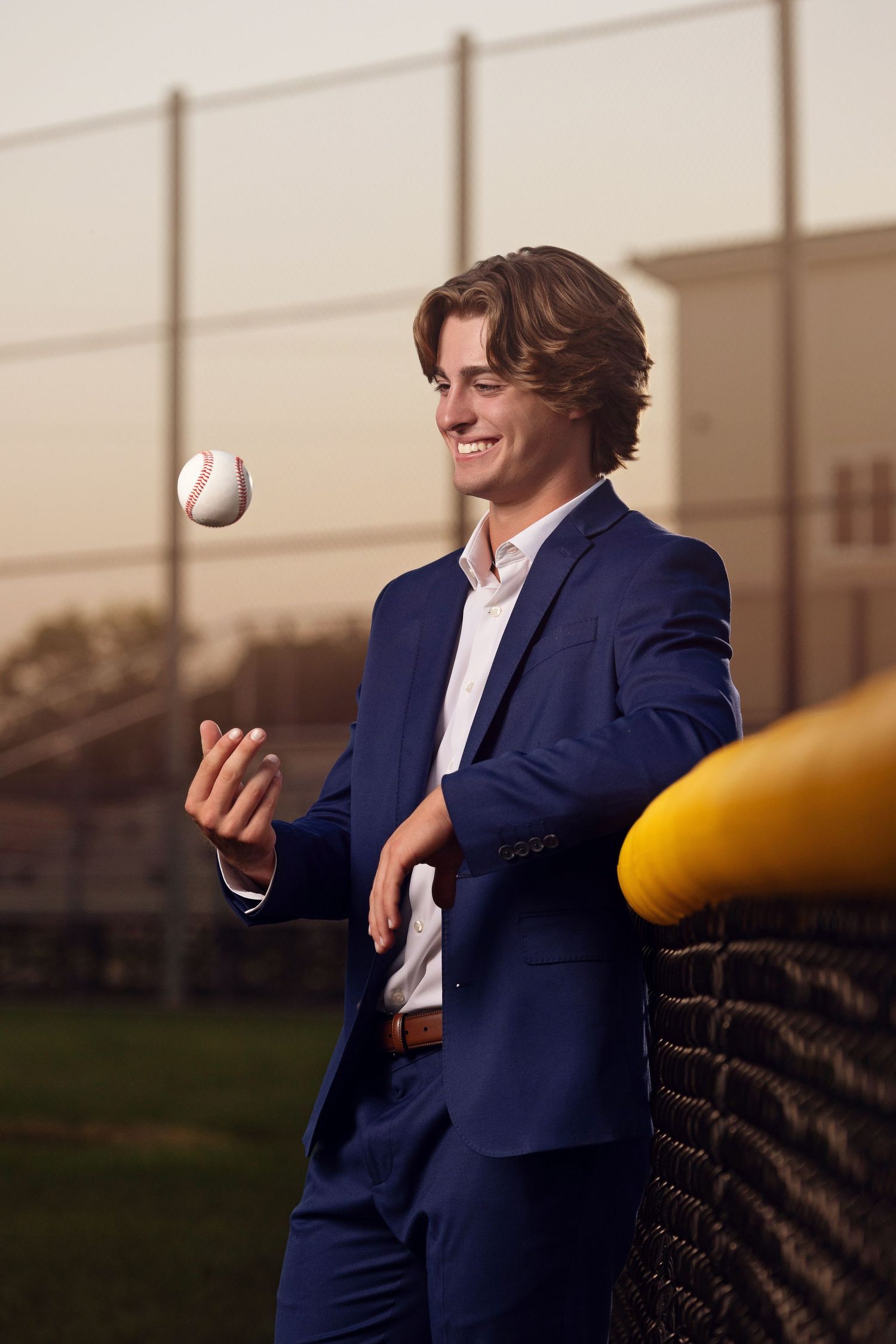 Person in navy suit jacket juggles multiple objects while standing outdoors in warm lighting.