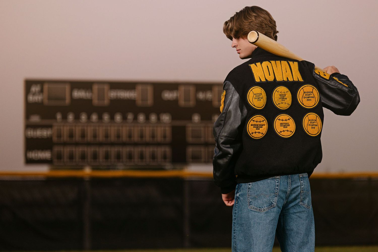 Person in a denim jacket with yellow patches bowls at a bowling alley lane.