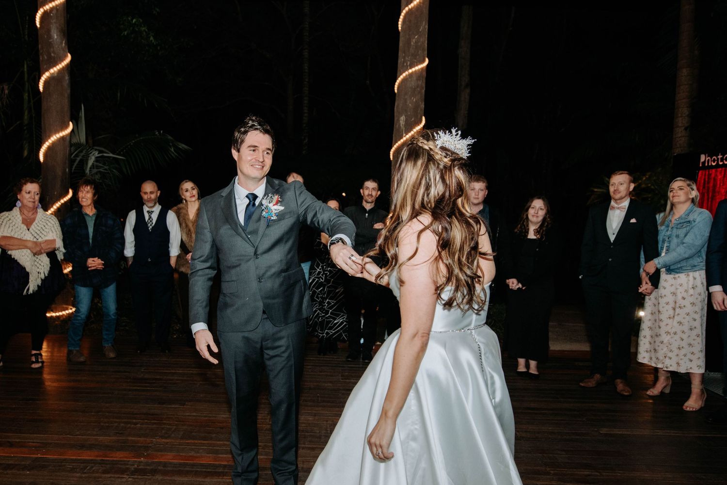 A couple shares their first dance at a reception with elegant spiral columns and watching guests.