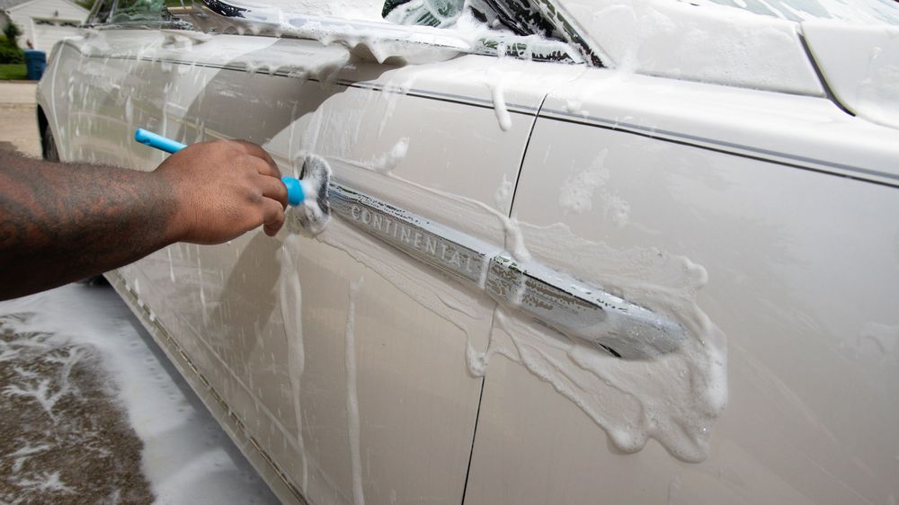 Hand applying car washing solution to white vehicle exterior.