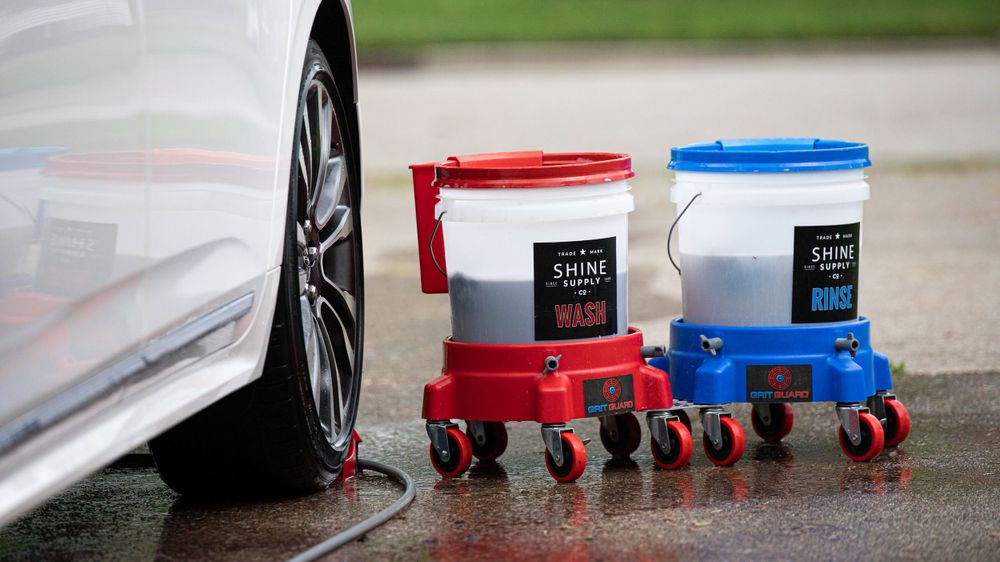 Red and blue detailing product buckets with wheels positioned next to car tire.