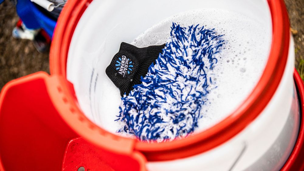Blue and white wash mitt floating in red detailing bucket filled with soapy water.