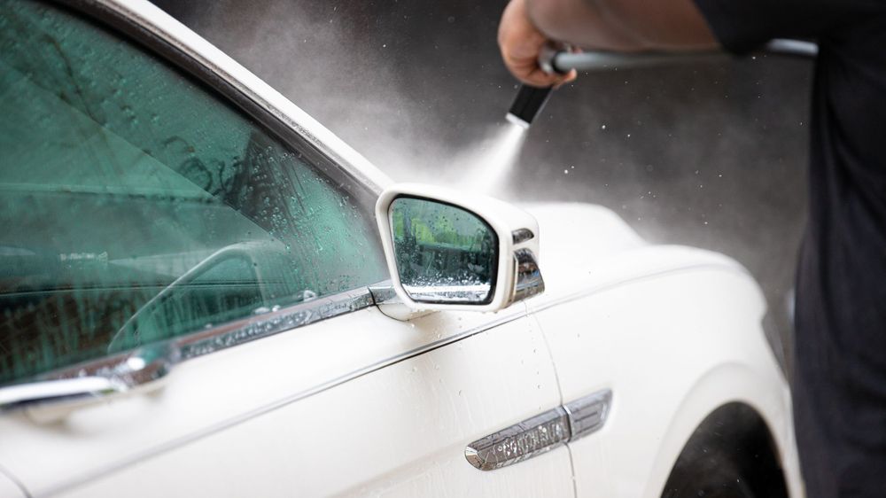 Detailed view of white car side mirror being cleaned with water spray.