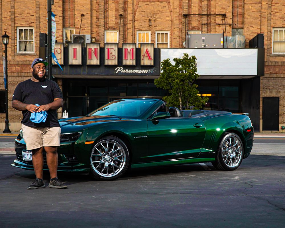 Green Chevrolet Camaro convertible parked in front of brick building at dusk.