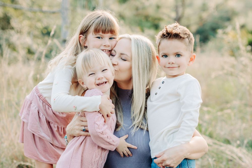 mom kissing her three children in a field