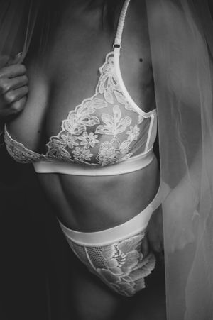 Black and white photo of a woman wearing floral lace lingerie set with a sheer veil draped over her shoulder.
