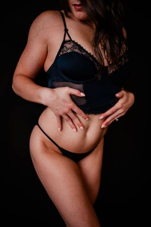 Artistic boudoir photo showing a figure in black lingerie against dark background.