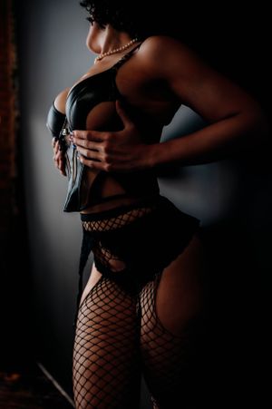 Artistic boudoir silhouette showing a figure in black lingerie and fishnet stockings against dark background.