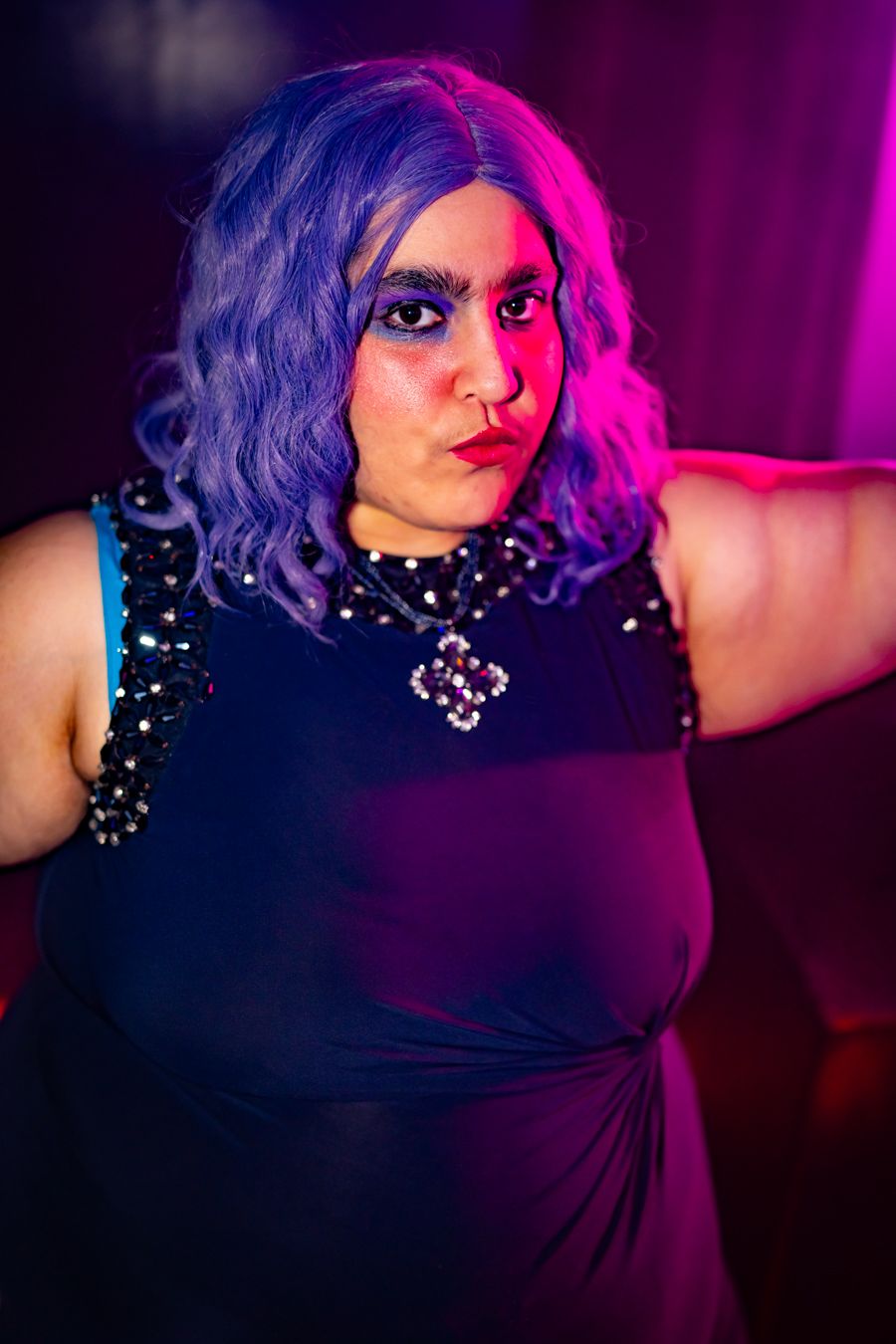 Theatrical portrait with dramatic pink and blue lighting of performer in sparkly black outfit.
