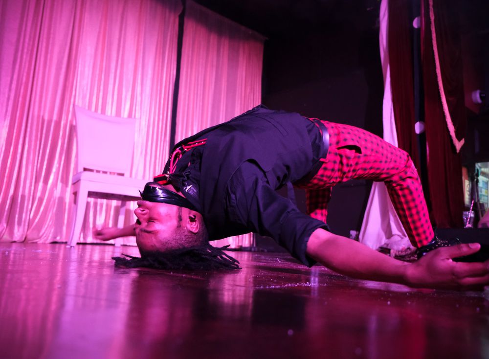 Performer in dark clothing on stage with pink curtains during an expressive dance move.