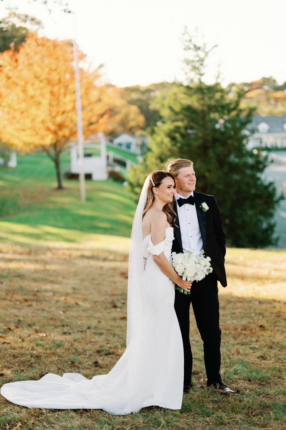 A romantic wedding couple shares tender moments in a golden autumn setting on a grassy hillside, their love illuminated by sunset.