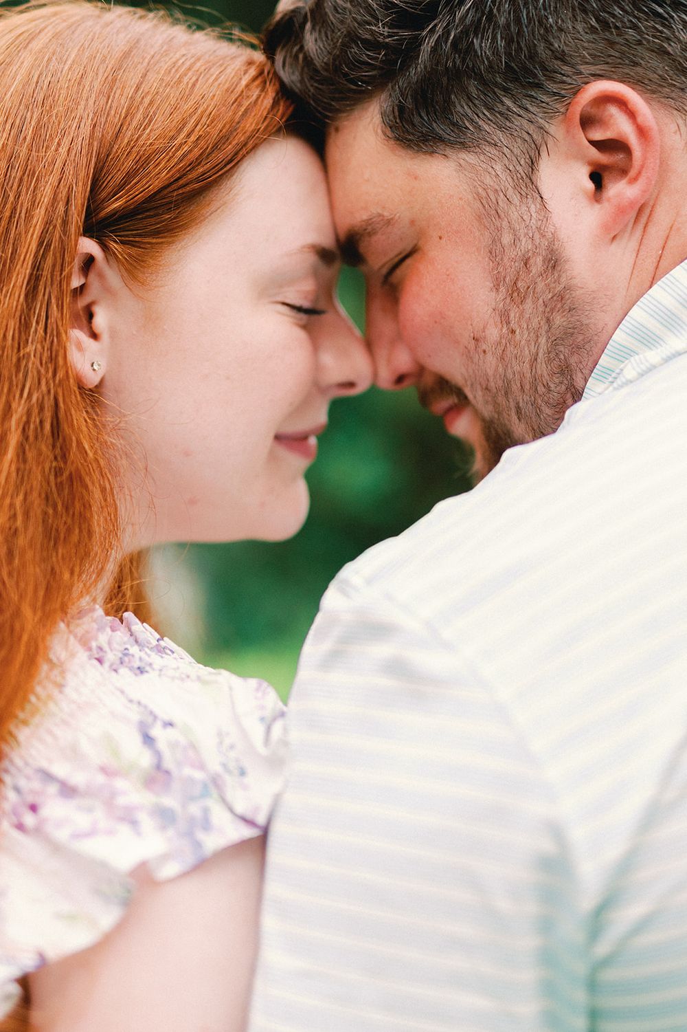 Close up romantic portrait of a couple touching foreheads tenderly against a green background.