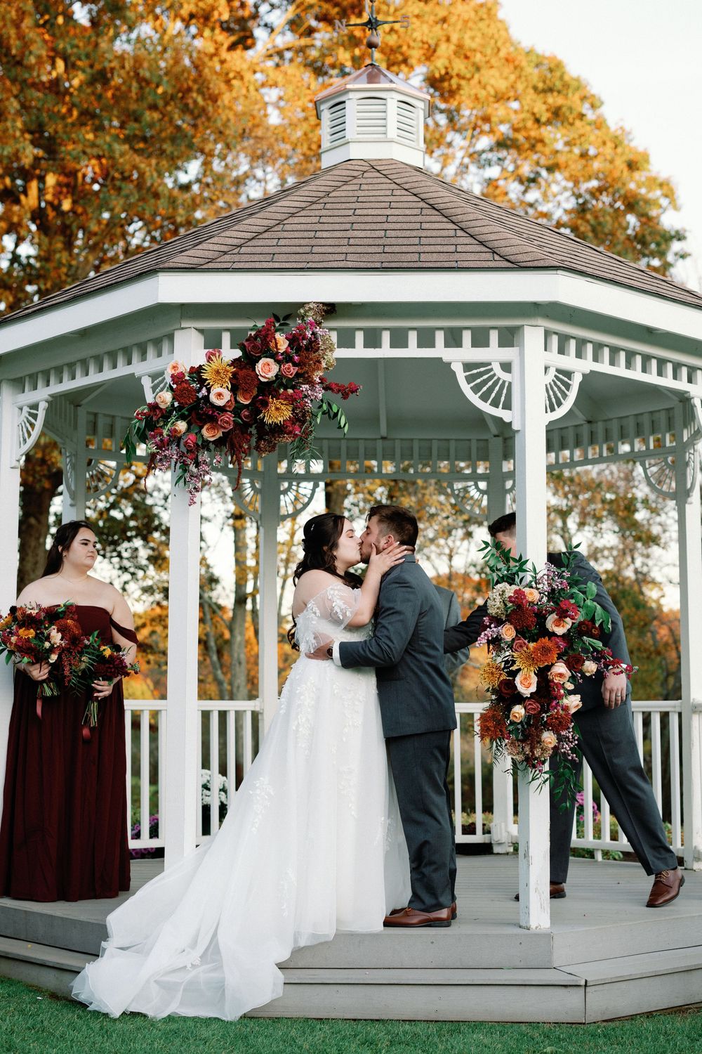 A romantic autumn wedding ceremony in a white gazebo decorated with burgundy and blush floral arrangements.