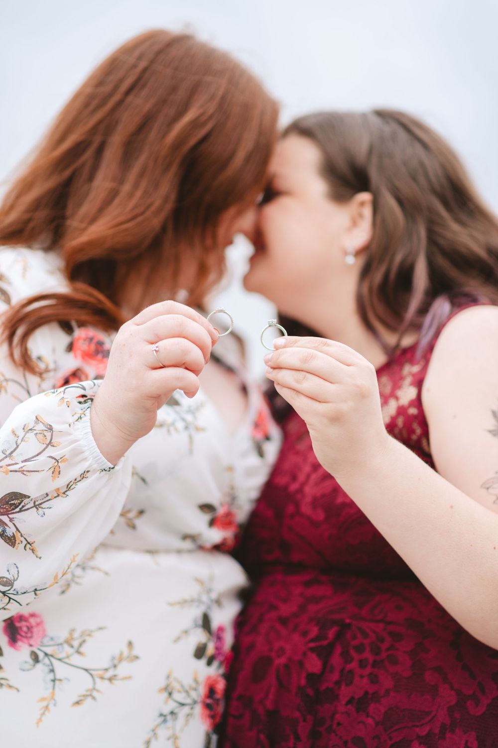 Two people in floral and burgundy dresses sharing a moment together outdoors.