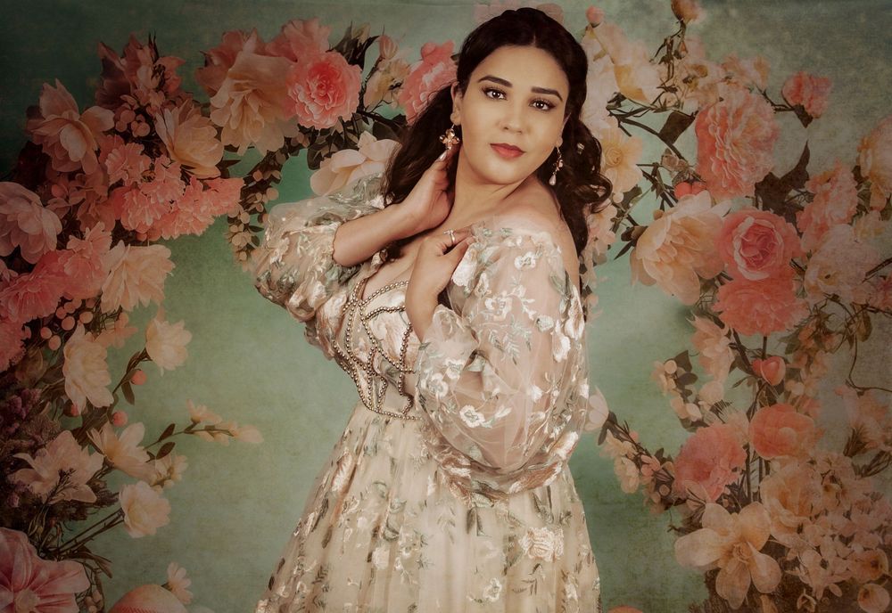 Figure in ethereal floral dress poses against a backdrop of coral roses and mint green tones.