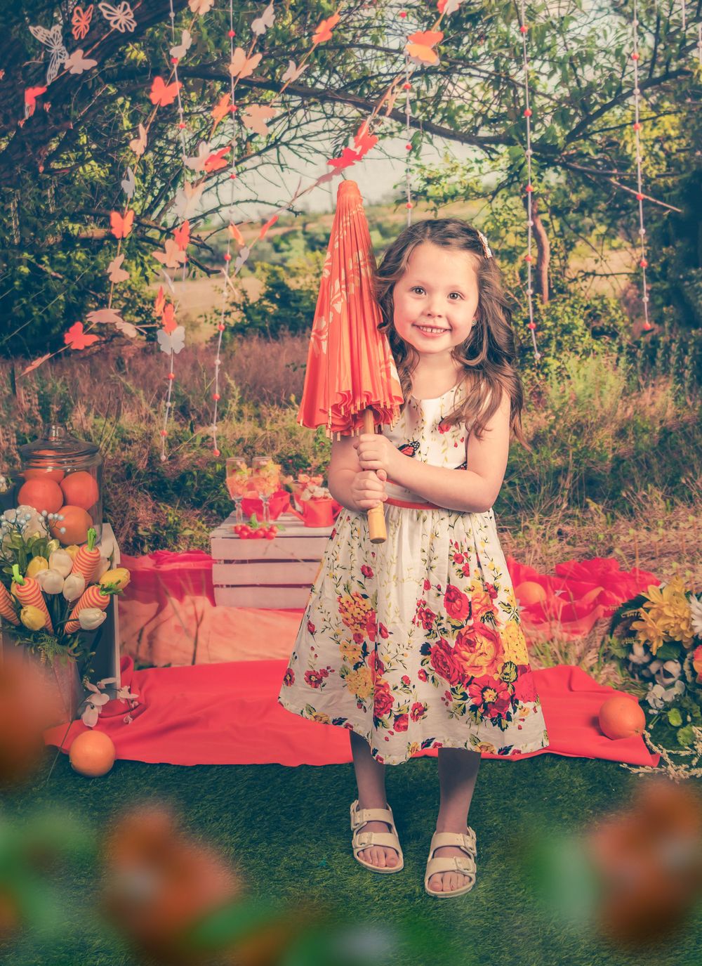 Garden photography scene with coral decorations and floral dress against a natural backdrop.