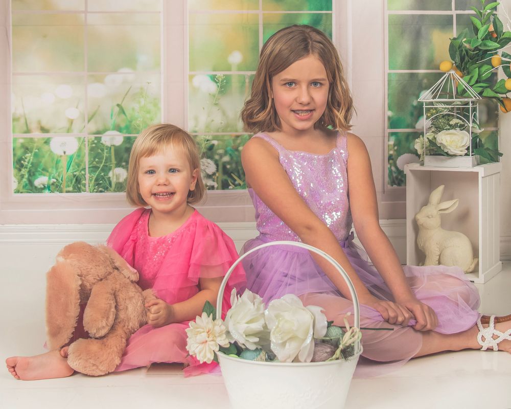Easter themed indoor portrait with basket of flowers and bunny decorations by sunny windows.