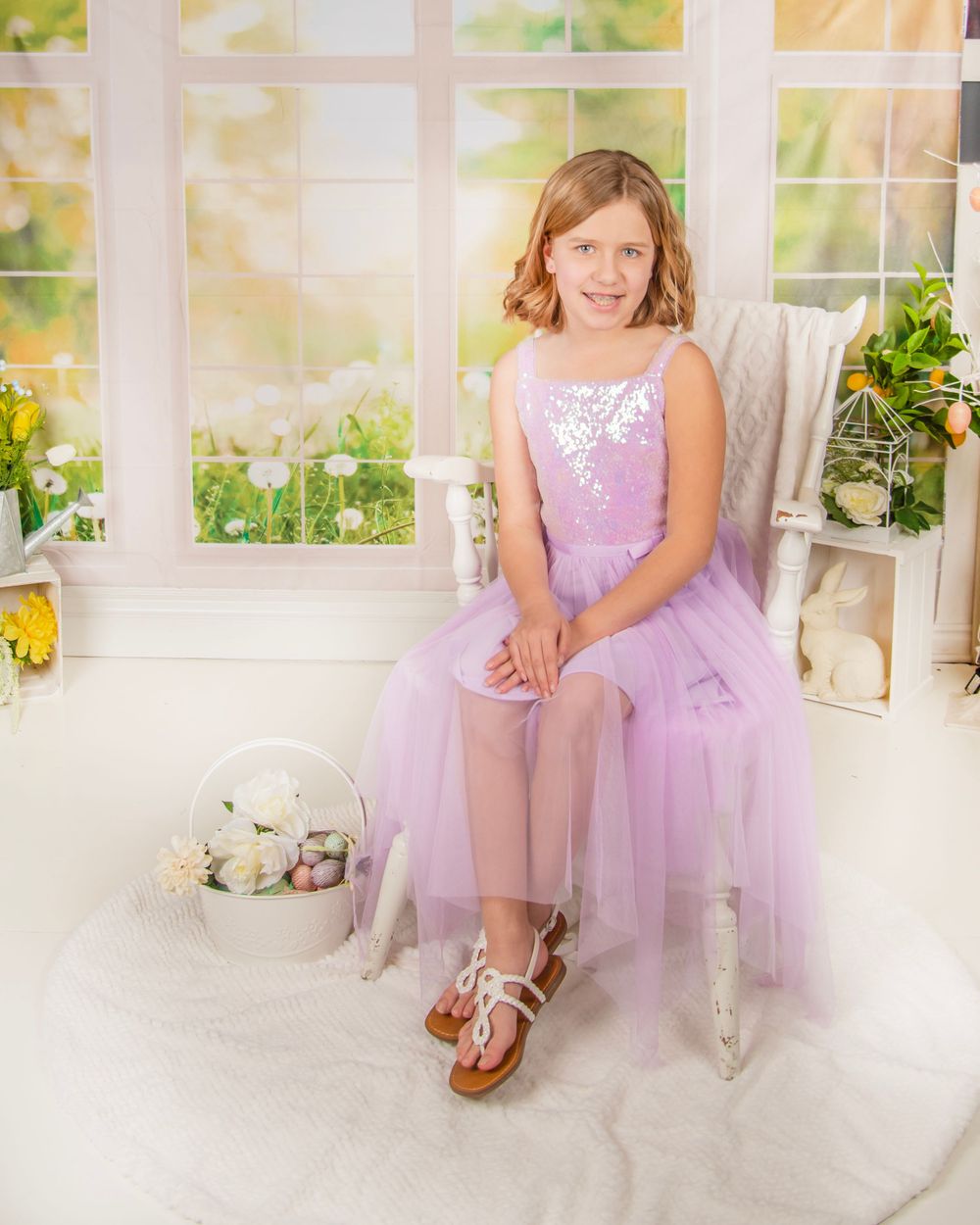 Portrait scene in a sunlit conservatory with lavender tulle dress and white chair.