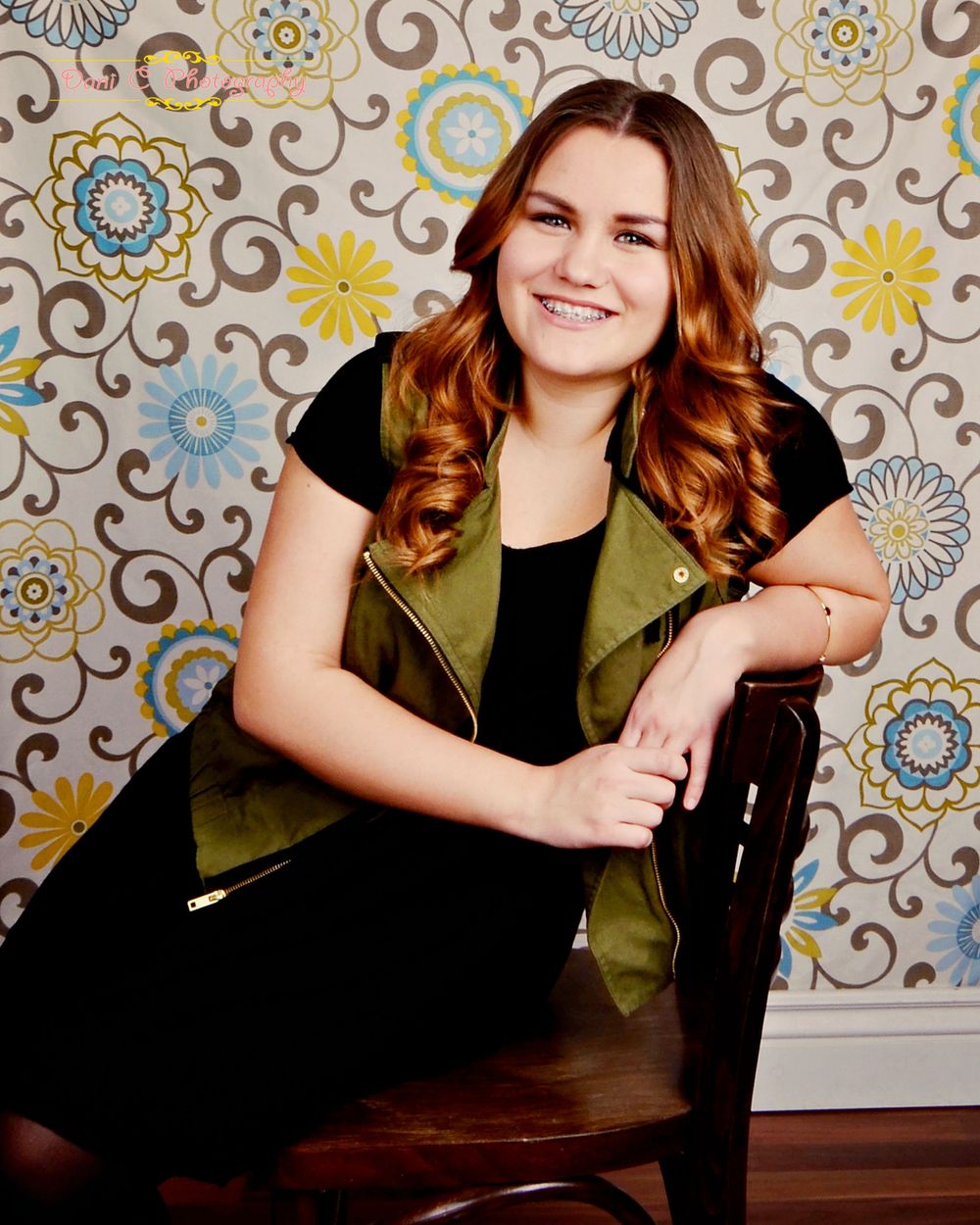 Studio portrait against floral wallpaper with vintage chair and bohemian styling.