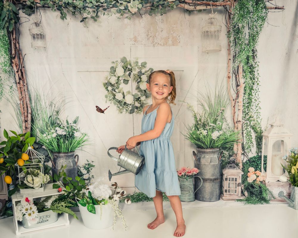 Garden themed portrait setup with vintage watering can and potted plants against white backdrop.