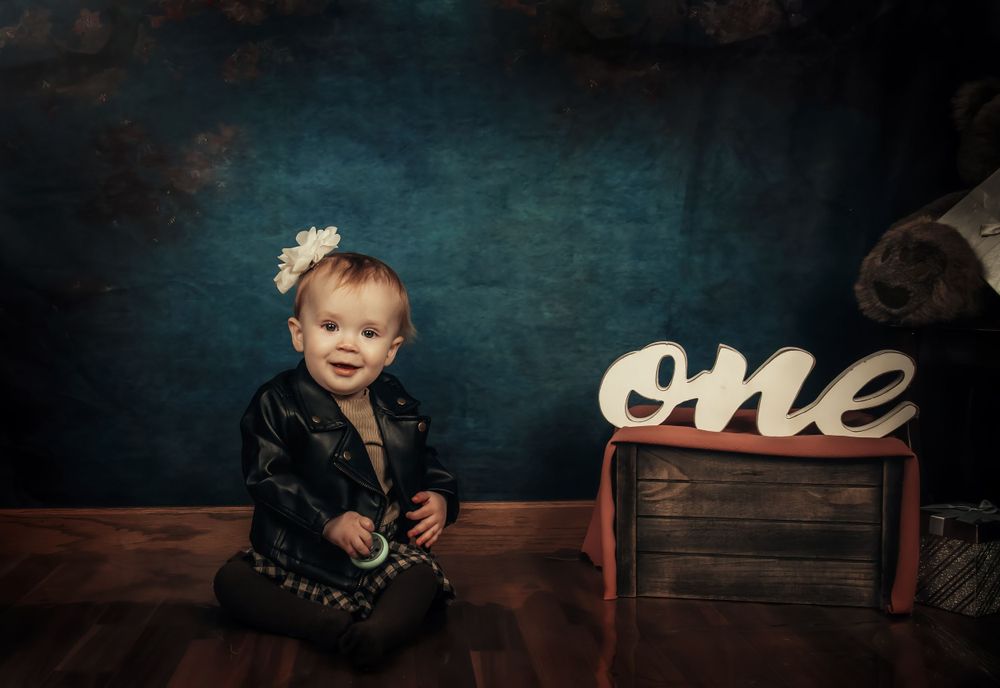Dark moody portrait with wooden box and 'one' text sign against chalkboard background.