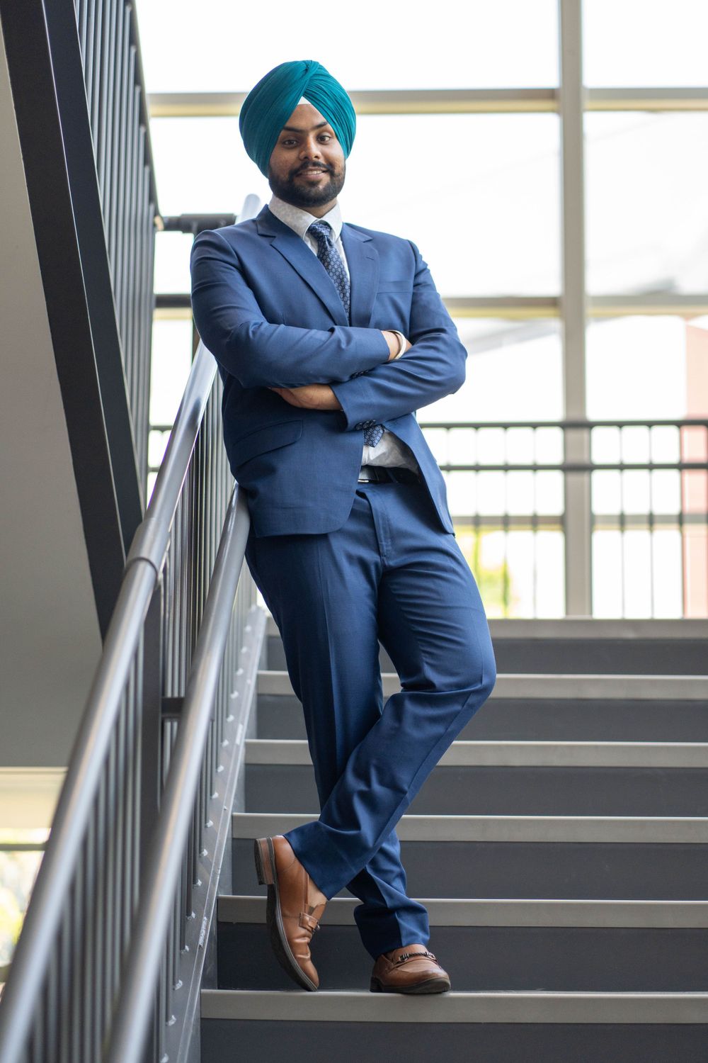 Professional in blue suit and turban posing on office staircase.