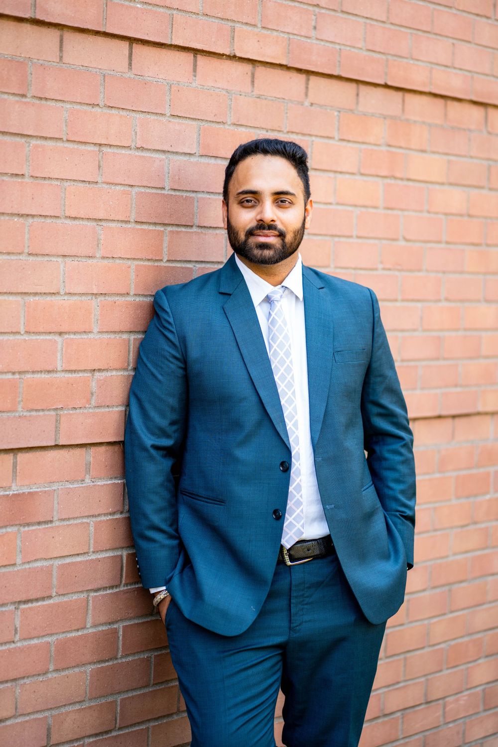 Professional portrait against brick wall in navy business suit.